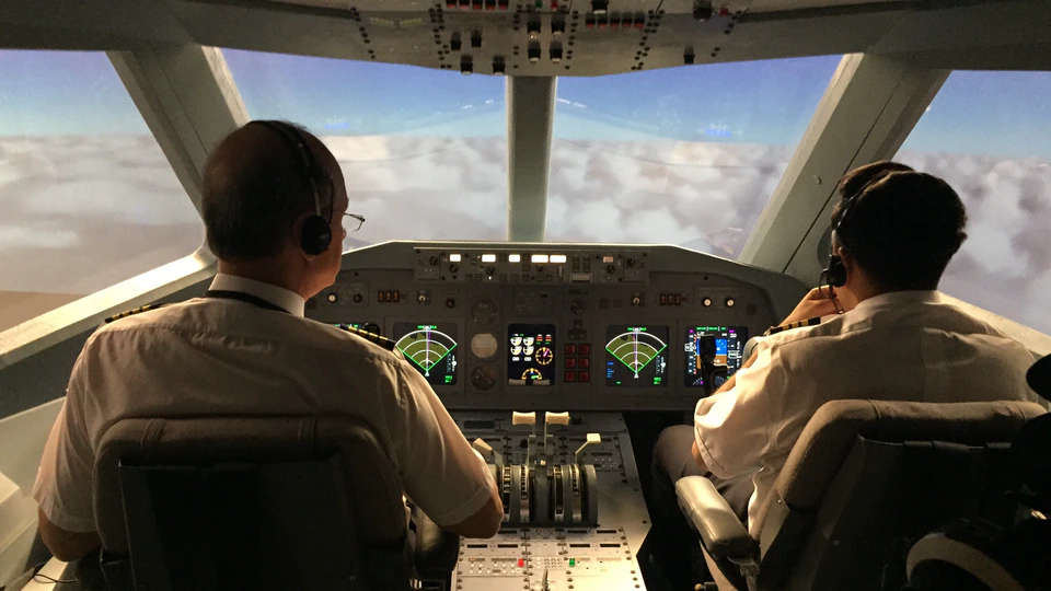 Two actors in a cockpit with clouds visible through the aircraft windows on the Ça Décolle! set.