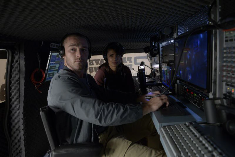 Actors surrounded by surveillance screens and controls inside the Quantico audio surveillance van.