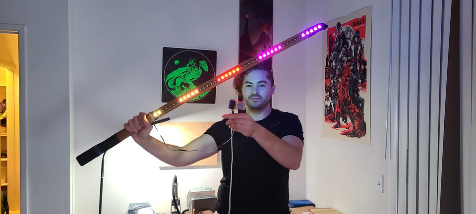 An early bokken lightsaber prototype held horizontally, with the exposed LED strip illuminated in several colors.