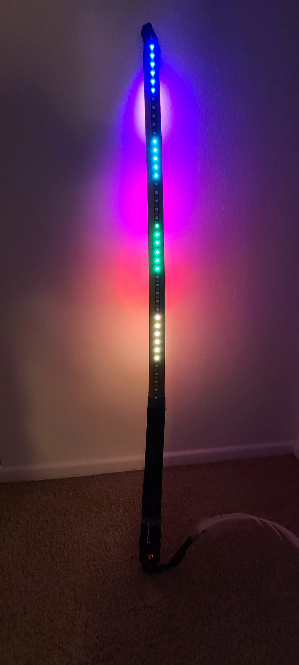 An illuminated bokken prototype leaning upright against a wall.