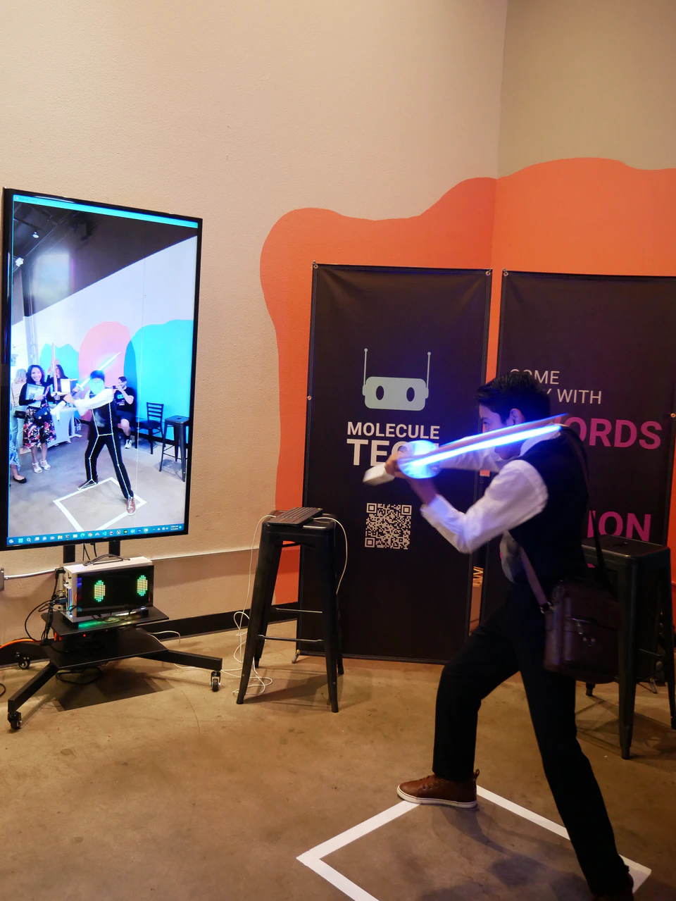 A visitor winding up an illuminated bokken beside the body-tracking display.