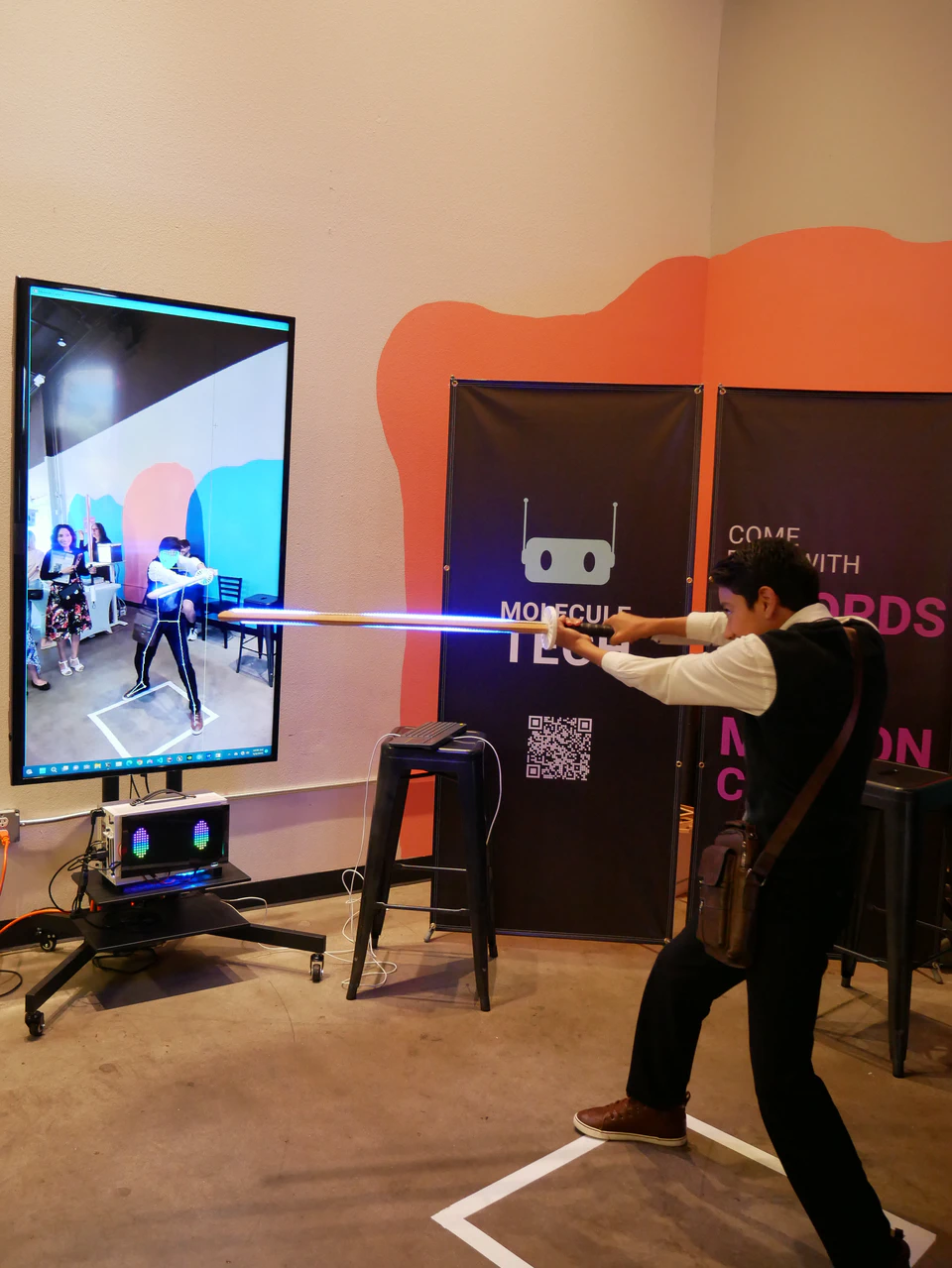 A visitor pointing an illuminated bokken toward the body-tracking screen.